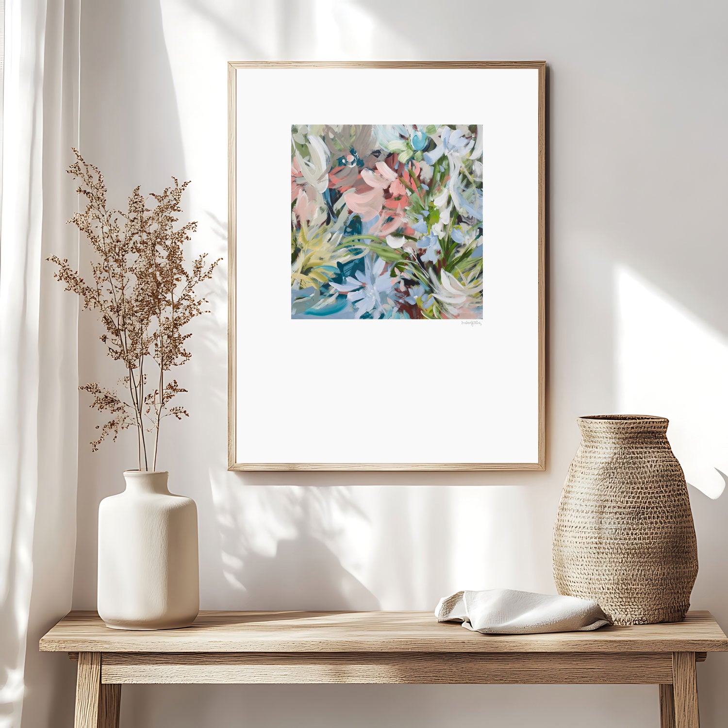 Colourful abstract flower paper wall art print in pastel shades of pink, blue, green, white and brown. Simple floral shapes layered in an expressionist style. Big white border surrounding the square flower design. Framed in a natural frame and hanging in a modern neutral lounge room.