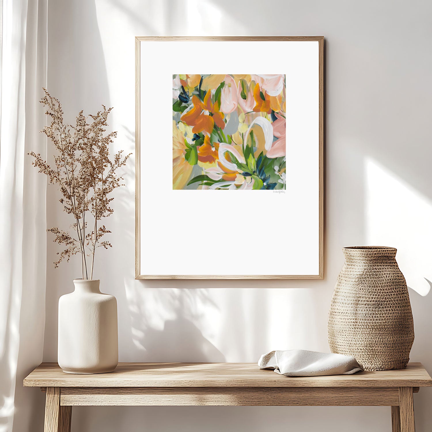 Modern abstract flower wall art print in soft shades of orange, green, warm yellow. Layered flower petals in an expressive style in a square format. Big white border surrounds the design. Framed in a natural frame and hanging on a contemporary neutral living room wall.