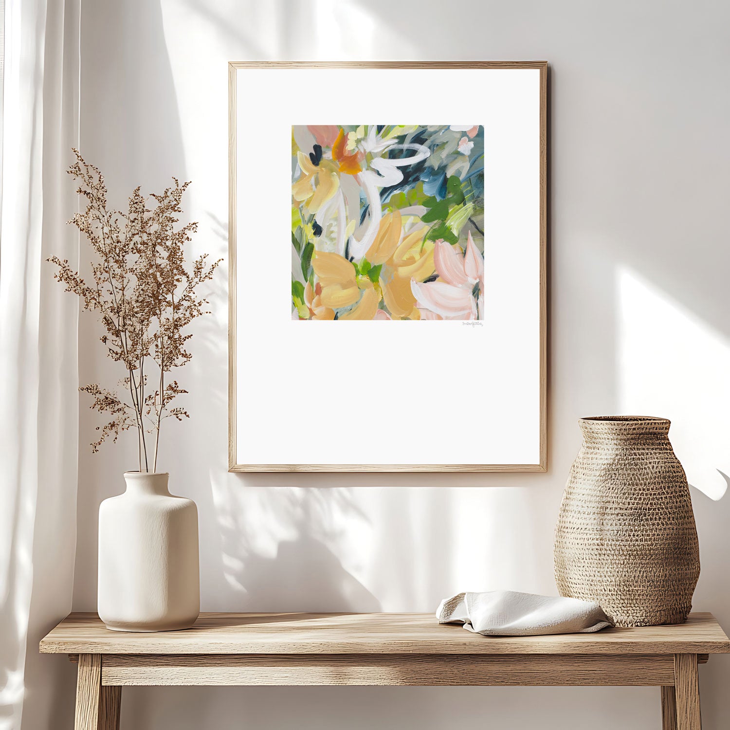 Modern abstract flower wall art print in soft shades of orange, green, warm yellow. Layered flower petals in an expressive style in a square format. Big white border surrounds the design. Framed in a natural frame and hanging on a contemporary neutral living room wall.
