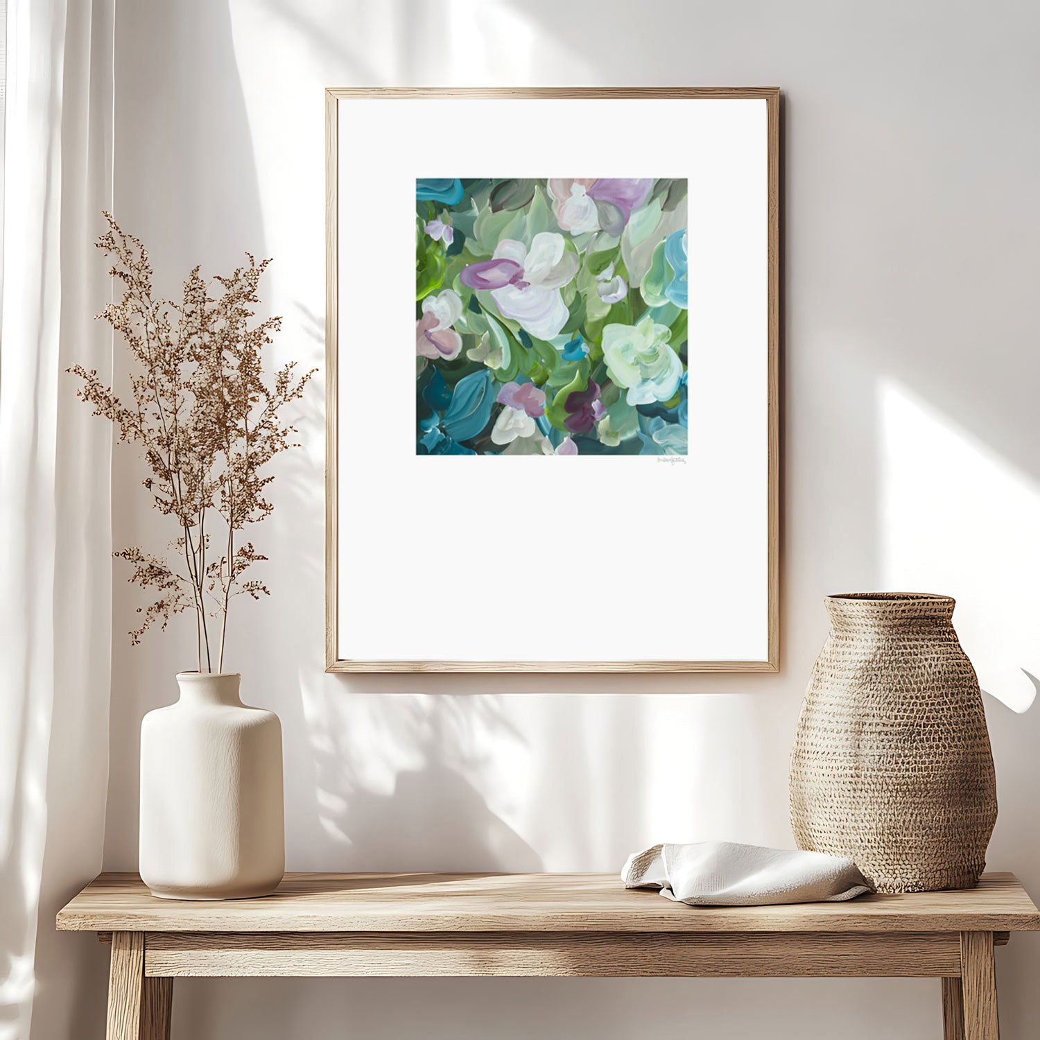 Beautiful feminine abstract floral wall art print in pastel shades of green, turquoise and pink. Simple floral organic shapes layered in a modern style. Big white border surrounding the square inner design. Framed in a natural frame and hanging in a natural inspired living room.