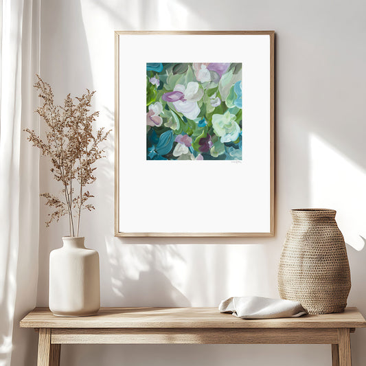 Beautiful feminine abstract floral wall art print in pastel shades of green, turquoise and pink. Simple floral organic shapes layered in a modern style. Big white border surrounding the square inner design. Framed in a natural frame and hanging in a natural inspired living room.