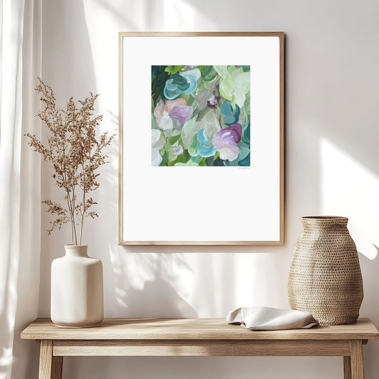 Beautiful feminine abstract floral wall art print in pastel shades of green, turquoise and pink. Simple floral organic shapes layered in a modern style. Big white border surrounding the square inner design. Framed in a natural frame and hanging in a natural inspired living room.