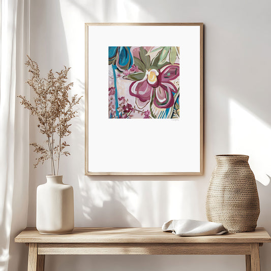 Modern eclectic flower abstract art print in pinks and turquoise. Bohemian inspired style of design of linear flower petal shapes in a fun flowing design. Big white border around the square shaped colourful design. Framed in a natural frame and hanging in a boho inspired living room.