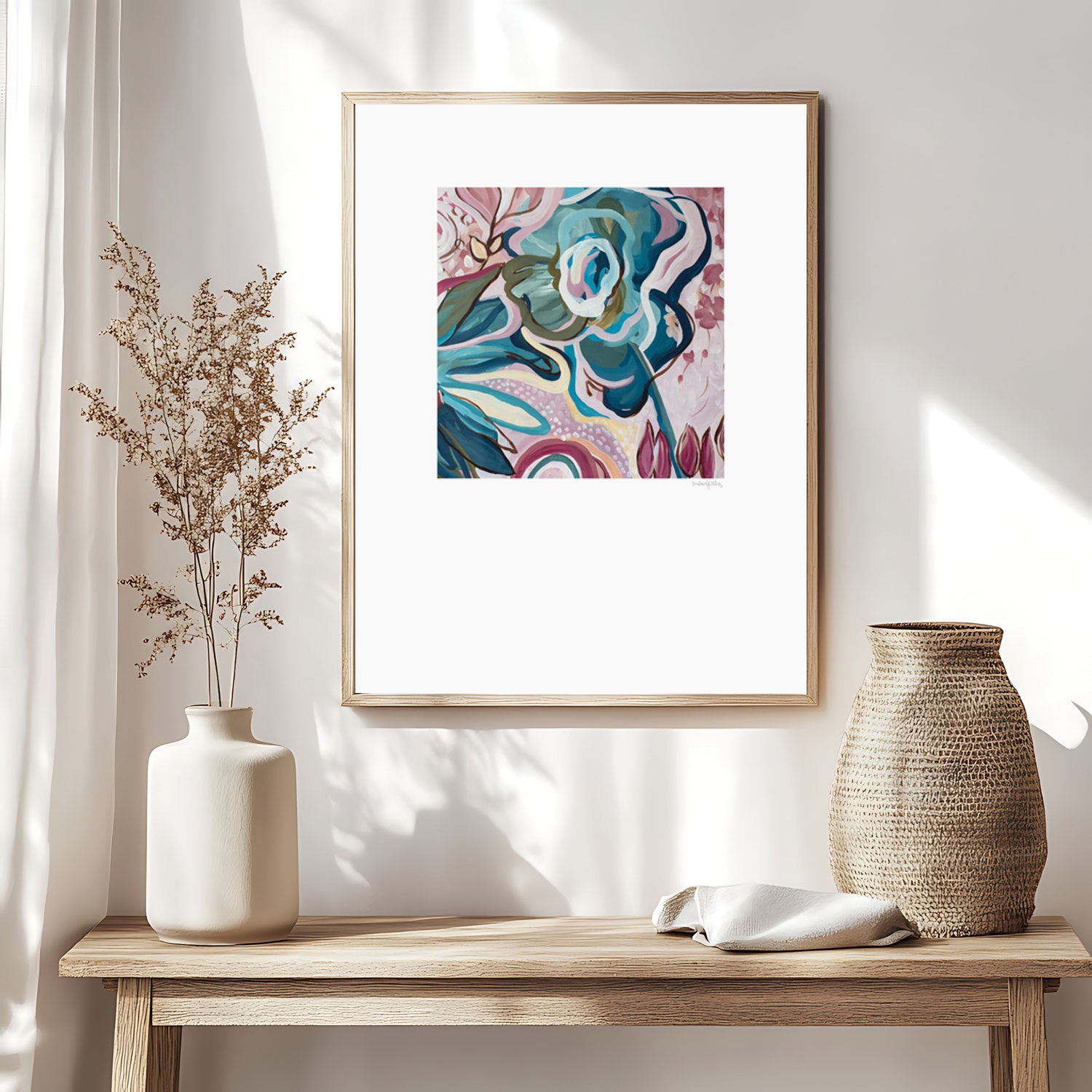 Modern eclectic flower abstract art print in pinks and turquoise. Linear flower petal shapes in a fun flowing design. Big white border around the square shaped colourful design. Framed in a natural frame and hanging on a modern neutral boho style living room wall.