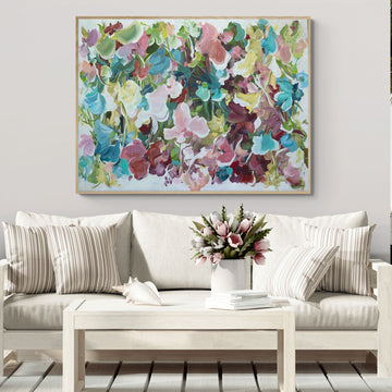 modern abstract floral artwork in multi colours of pink, light blue, green, burgundy and yellow with a white background. Hanging in a living room with a white couch and white table.