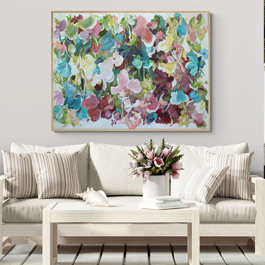 modern abstract floral artwork in multi colours of pink, light blue, green, burgundy and yellow with a white background. Hanging in a living room with a white couch and white table.
