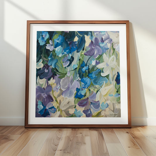 Modern blue and purple abstract floral art print leaning against a living room wall in a natural frame.
