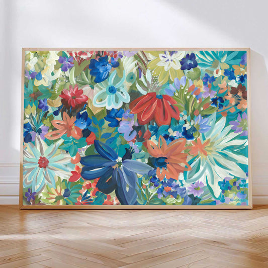 Colourful blue, red, green and orange abstract flower canvas art print leaning against a wall with a natural frame.