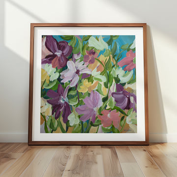 Colourful flower fine art print in a modern layered style with purple, green, pink, blue and warm yellow colours. Framed in a natural frame leaning against a lounge room wall.