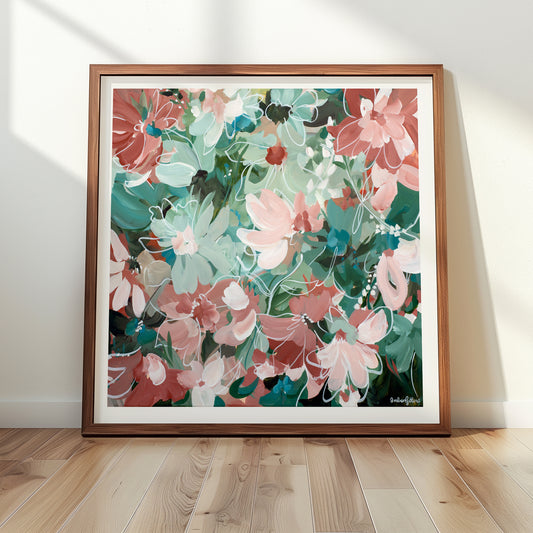 Framed abstract floral art print in greens and pinks leaning on a wall with wooden floor
