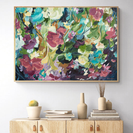 Colourful modern abstract floral wall art print. Expressionist contemporary style of floating flower petals and leaves. Framed in a natural frame hanging against a living room wall.