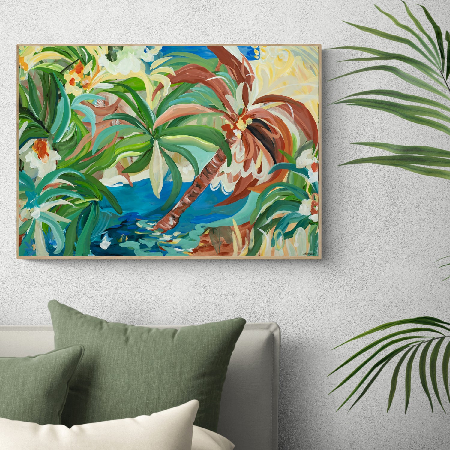 Colourful abstract wall art print of a modern tropical oasis scene depicting palm trees, tropical flowers and water. Framed in a natural frame leaning against a living room wall.