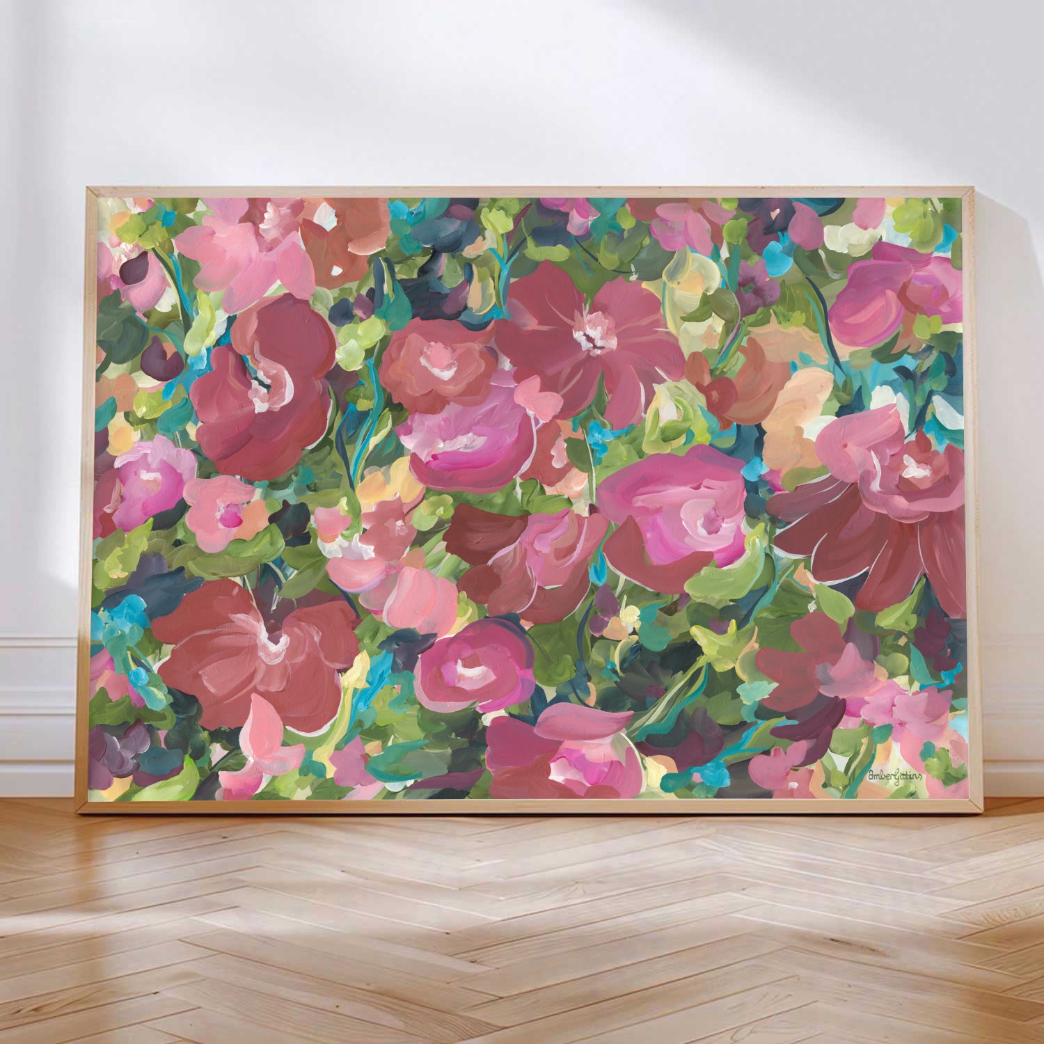 Pretty red and pink and green abstract flower canvas print leaning against a living room wall with a natural frame.