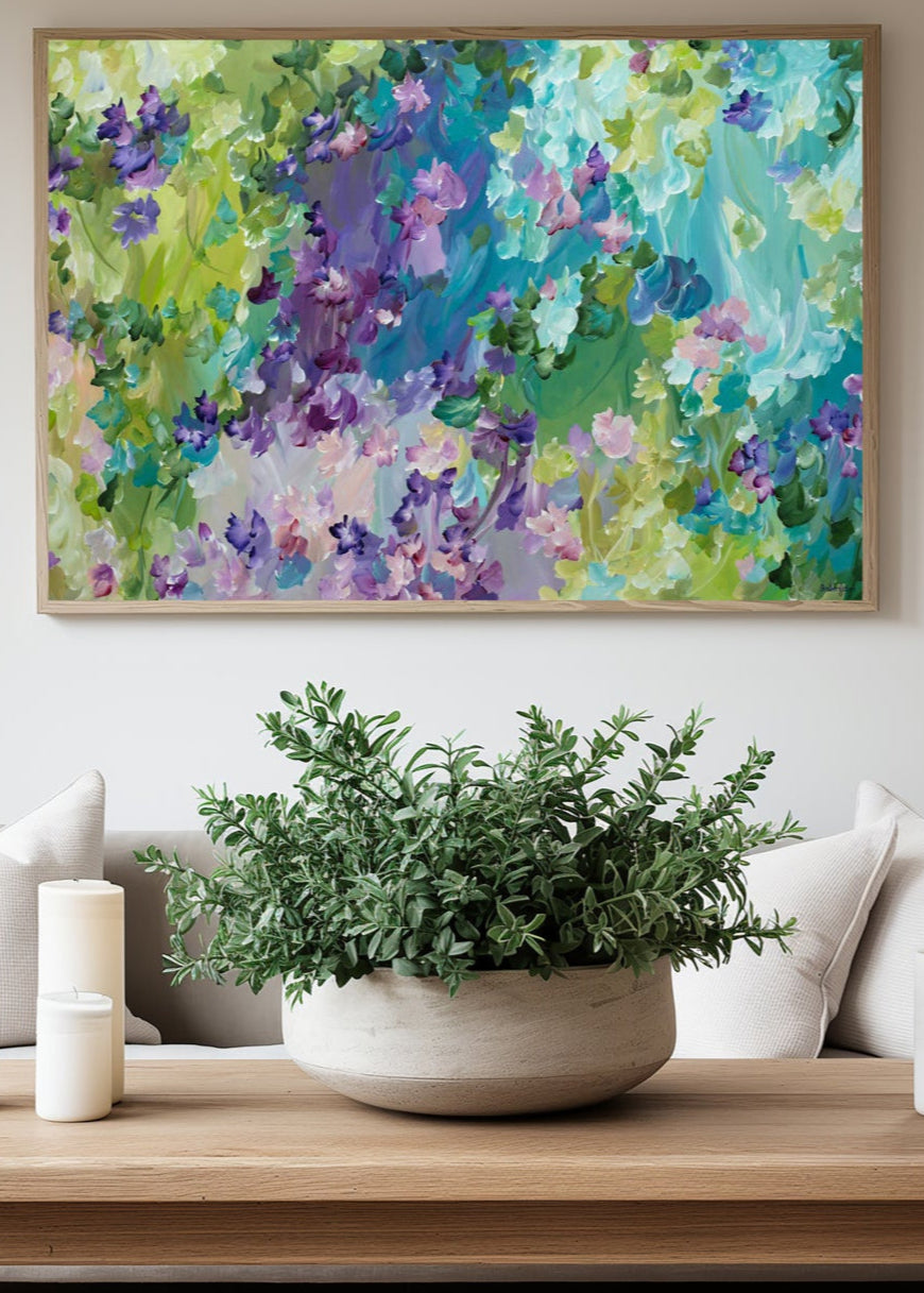 Colourful blue, green and purple abstract flower  fine art canvas print hanging in a neutral living room with a white lounge.