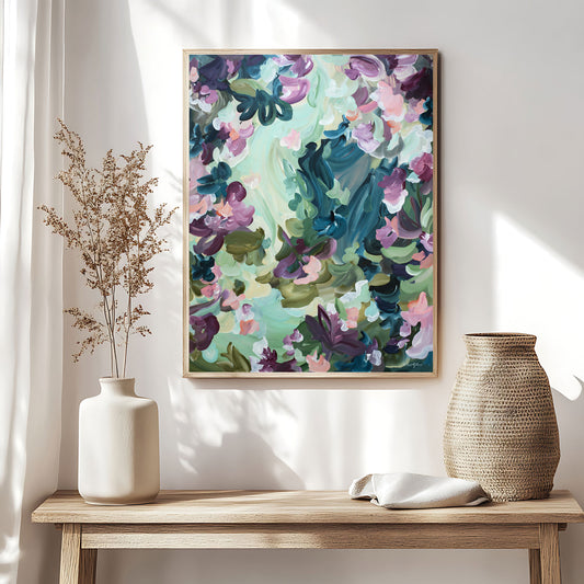 Modern abstract  fine art canvas print of floating flower petals in spearmint, purple, greens and dark blue. In a natural frame hanging against a living room wall.