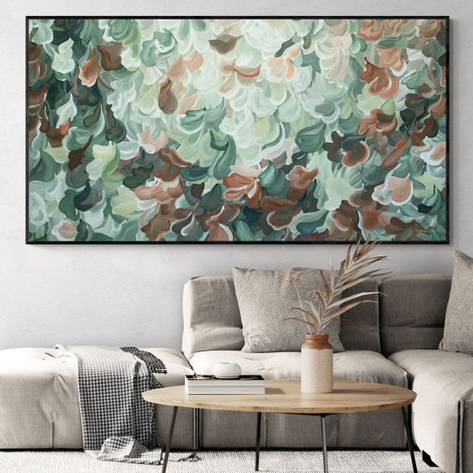 Large green and brown abstract nature painting with a black frame. Hanging in a natural coloured living room with a beige lounge chair.