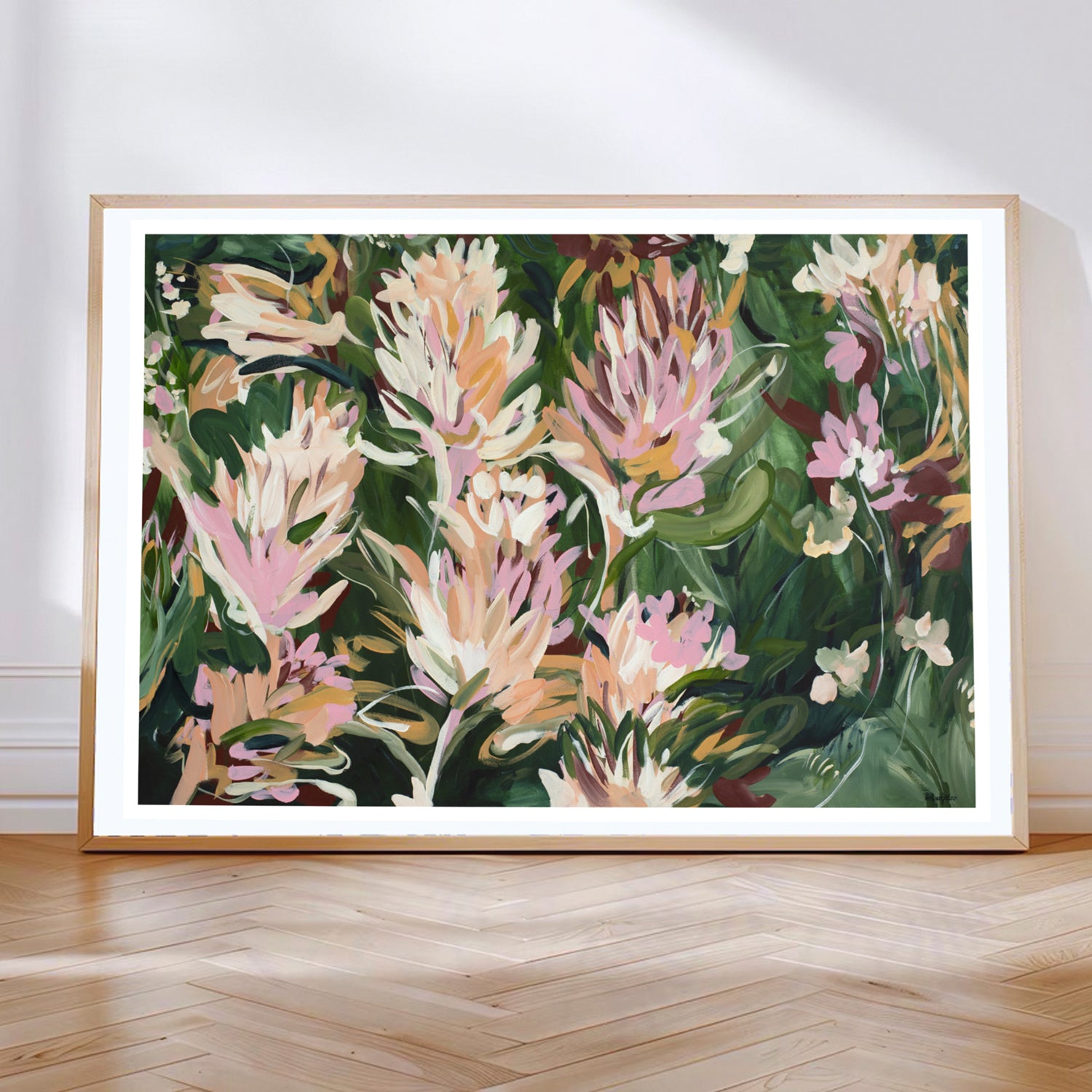 Colourful contemporary abstract protea flower wall art print in greens, pinks and warm orange yellow. Framed in a natural oak frame leaning against a living room wall.