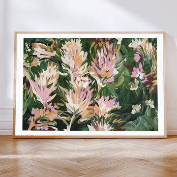 Colourful contemporary abstract protea flower wall art print in greens, pinks and warm orange yellow. Framed in a natural oak frame leaning against a living room wall.