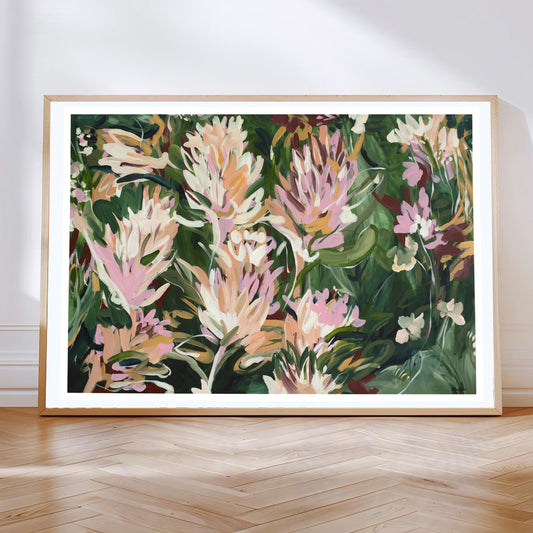 Colourful contemporary abstract protea flower wall art print in greens, pinks and warm orange yellow. Framed in a natural oak frame leaning against a living room wall.