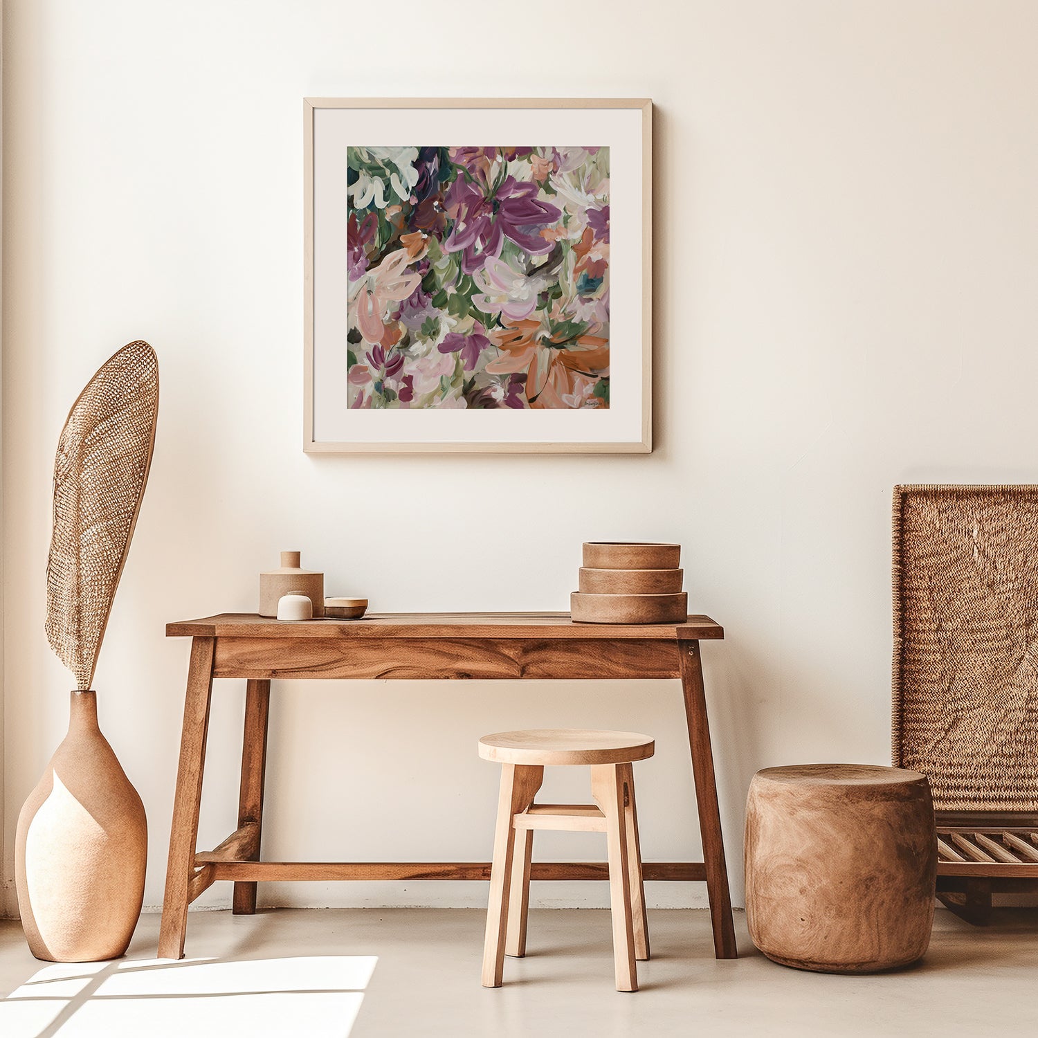 Colourful modern abstract flower fine art wall print in warm tones of red, burgundy, pink, orange and green. Layers of flowing brushstrokes showing linear flower and petal shapes. Framed in a white frame, leaning against a living room wall.