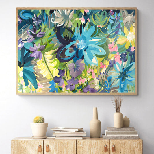 Colourful abstract fine art canvas print of tropical flowers with one big blue one and lots of little flowers. With a natural frame hanging on a living room wall.