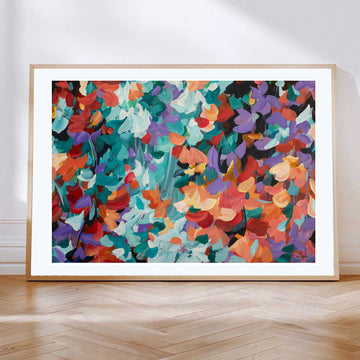 Bold and bright abstract art print in a modern abstract style of floating flower petals in red, orange, turquoise and purple. Leaning against a wall with a natural frame.
