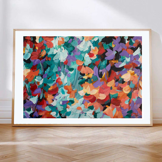 Bold and bright abstract art print in a modern abstract style of floating flower petals in red, orange, turquoise and purple. Leaning against a wall with a natural frame.