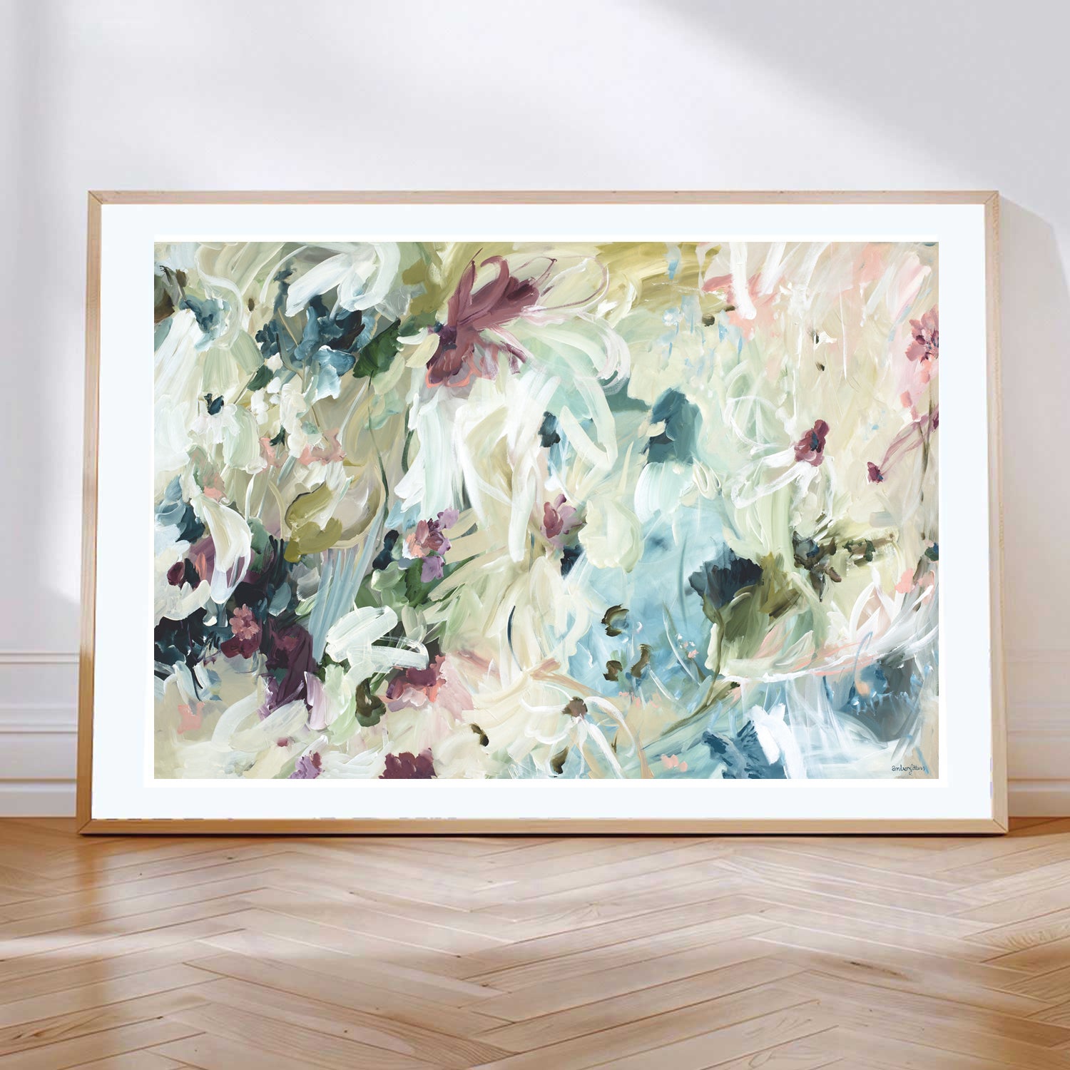 Modern neutral abstract flower wall art print. Minimal and contemporary style in beige, creams, with hints of green, turquoise and burgundy. Framed paper print in a natural frame leaning against a living room wall.