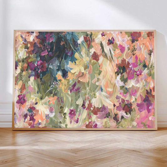 Colourful abstract wildflower print in pinks, orange, yellow and greens leaning against a wall with a natural frame.