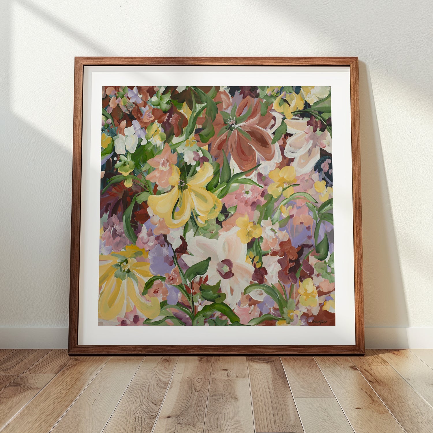 Natural and earthy wildflower abstract wall art print in neutral tones of brown, apricot, green, lilac and yellow. Layers of flower petals in a modern style. Framed in a natural frame , leaning against a living room wall.