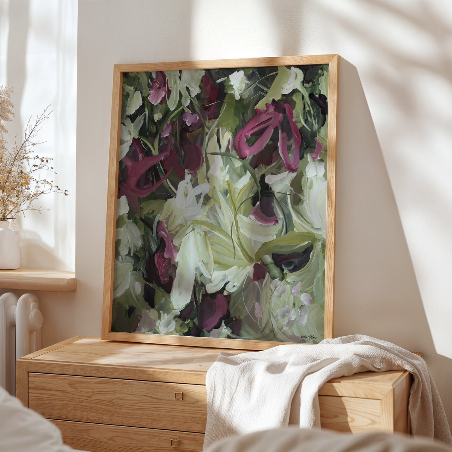 Modern wildflower abstract wall art print in contemporary colour palette of burgundy, white and green. Expressive organic flowing petal and leave shapes in layers. Framed wall art print in a natural frame leaning on a cupboard in a bedroom.