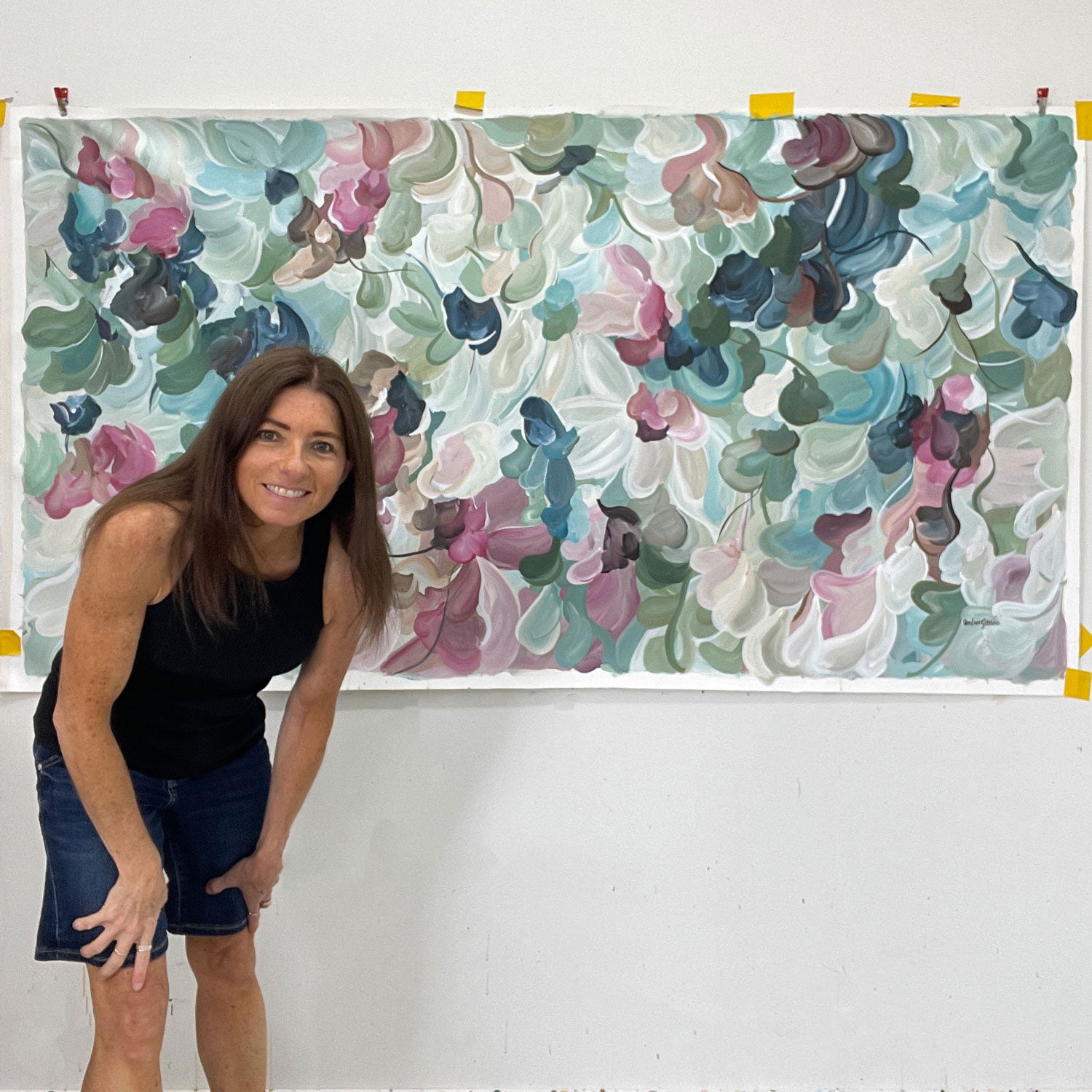 Artist Amber Gittins standing next to a large floral patterned original artwork on a white wall.
