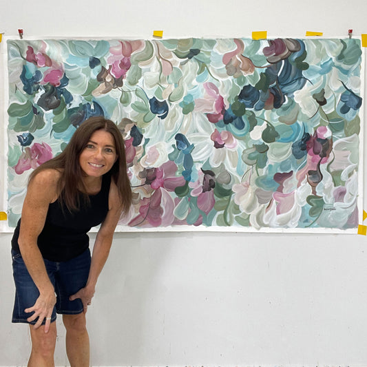 Artist Amber Gittins standing next to a large floral patterned original artwork on a white wall.