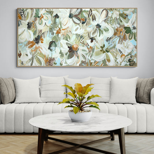 Floral painting above a white sofa with a coffee table and plant in a living room setting.