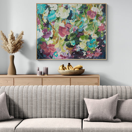 Colourful modern abstract floral wall art print. Expressionist contemporary style of floating flower petals and leaves. Framed in a natural frame hanging against a living room wall.