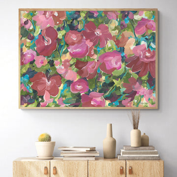 Colourful modern red and pink abstract botanical wall art print in a contemporary impressionist style. Framed in a natural frame and hanging against a living room wall.