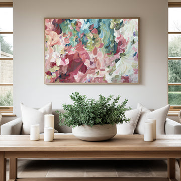 Modern impressionist style abstract flower art print in salmon pinks and greens hanging against a living room wall.