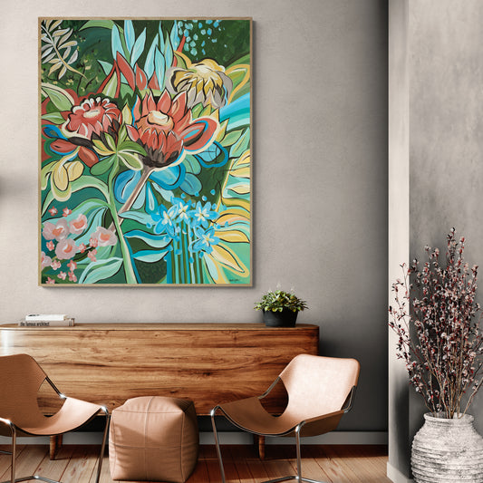 Colorful floral Protea painting on a wall above a wooden console table with chairs and decor.