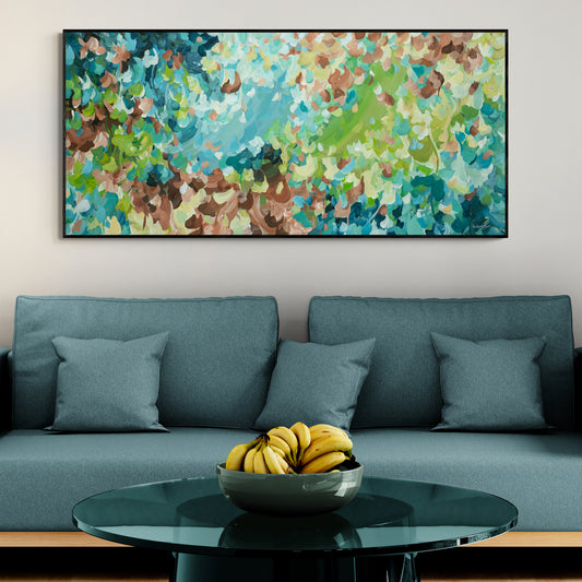 Living room with a blue sofa, colourful abstract painting, and a bowl of bananas on a glass table.