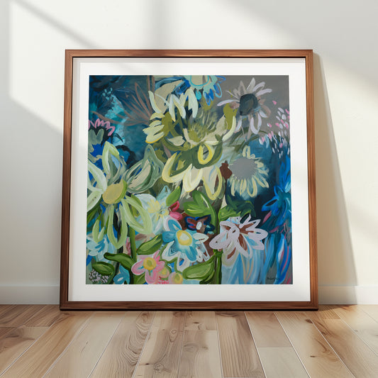 Contemporary square abstract flower fine art print in multi colours. Inspired by sunflowers in the moonlight. Layers of organic flowing shapes and colours in a playful style. Framed in a wood frame leaning against a wall.